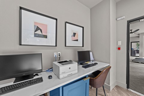 A modern office with a desk, two monitors, a laptop, and two framed pictures on the wall.