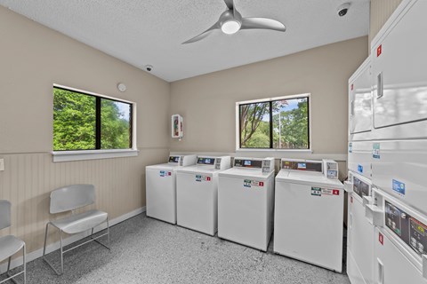 A room with a row of washing machines and a fan.