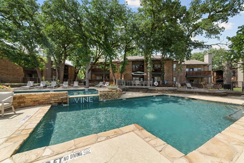 A pool surrounded by trees and a stone wall with the word Vine on it.