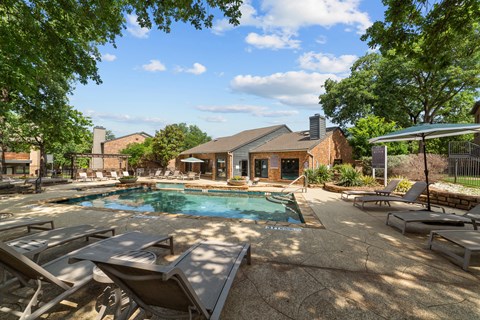 A pool surrounded by lounge chairs and trees.
