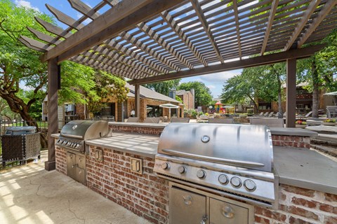 A large outdoor grill is under a pergola in a backyard.