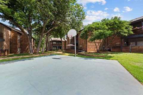 A basketball court is surrounded by trees and brick buildings.