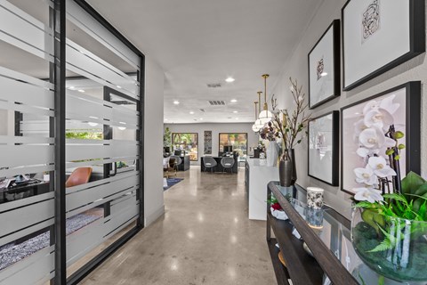 A modern interior with a long hallway, a glass table with flowers, and framed pictures on the wall.