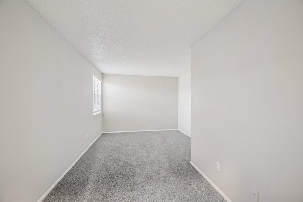 A spacious empty room with carpeted floor and white walls.