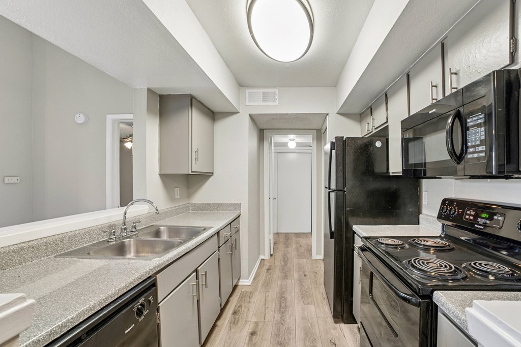 A kitchen with black appliances and a wooden floor.