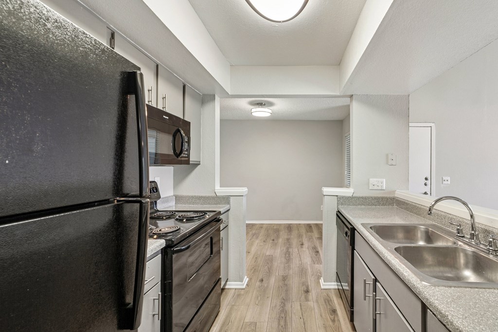A black refrigerator is in a kitchen with wood floors and stainless steel appliances.