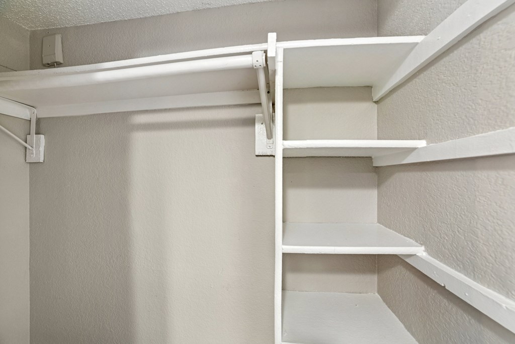 A white shelving unit with four shelves is mounted on a white wall.