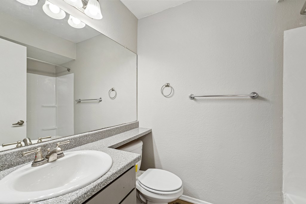 A bathroom with a toilet, sink, mirror, and towel rack.