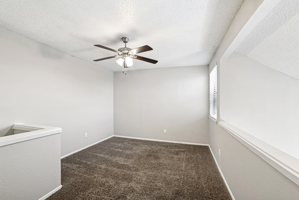 A room with a ceiling fan and carpeted floor.