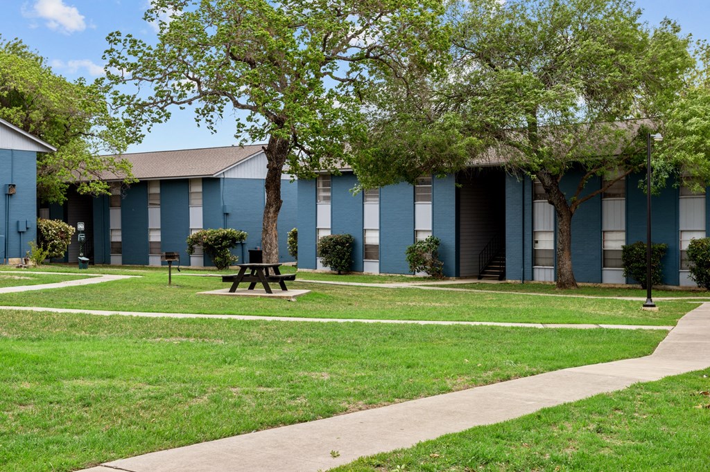 a picnic table sits in a grassy area in front of a blue building  at Sunset Heights, San Antonio, 78209