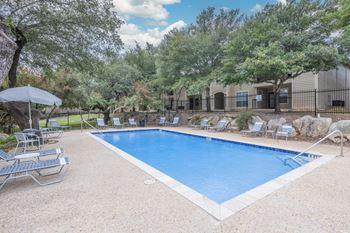 A pool surrounded by trees and chairs.
