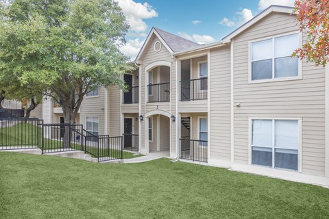 A beige two-story apartment building with a black fence and a green lawn.