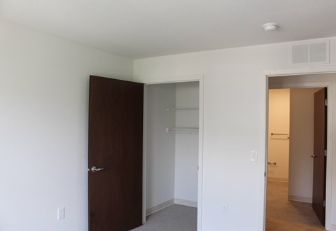 A white bedroom with a brown door and a white wall.