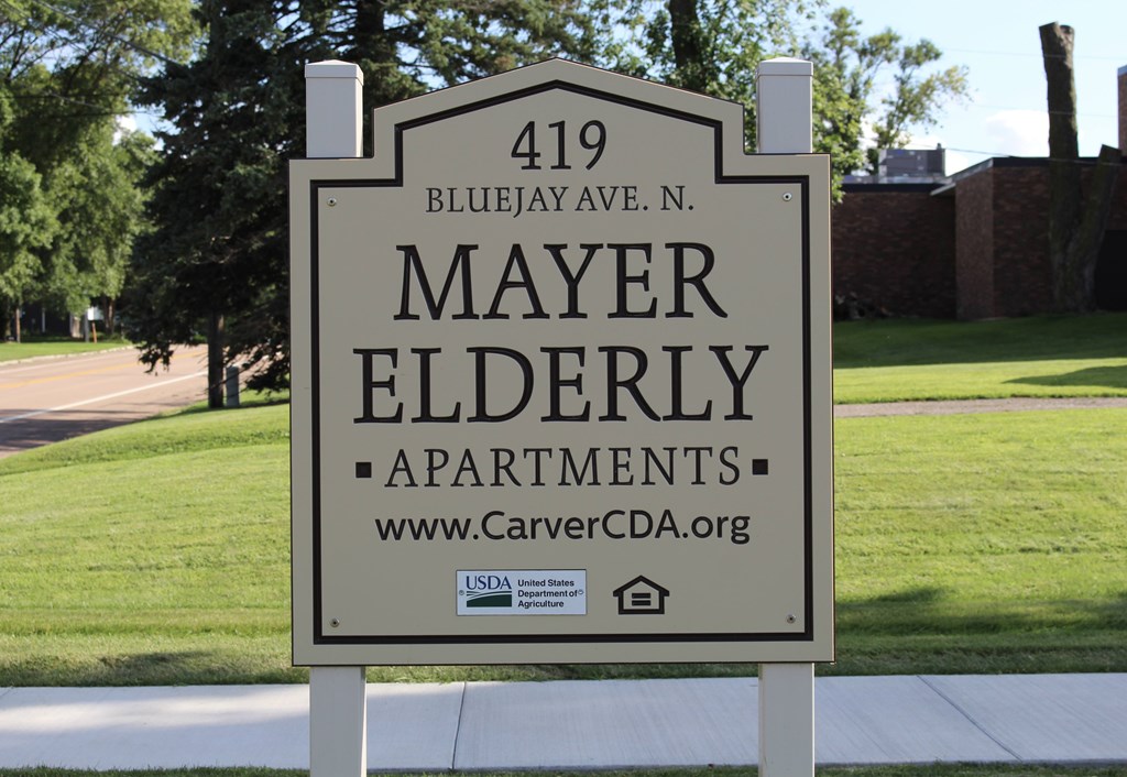 A sign for Mayer Elderly Apartments stands on a sidewalk.