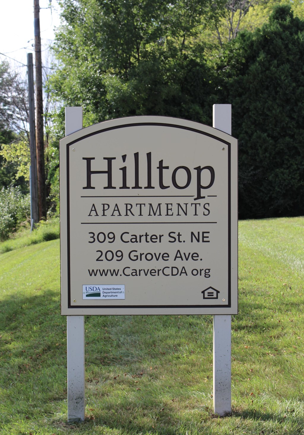 A sign for Hilltop Apartments is displayed in front of a green lawn.