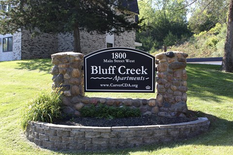A sign for Bluff Creek Apartments is displayed in front of a building.