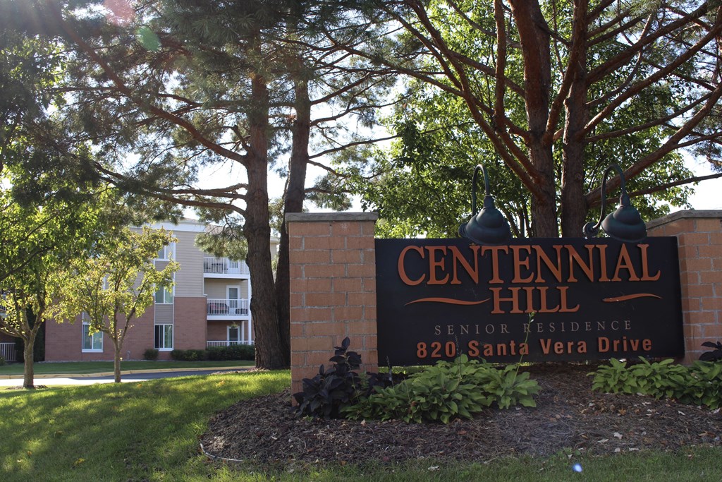 A sign for Centennial Hill Senior Residence stands in front of a tree.