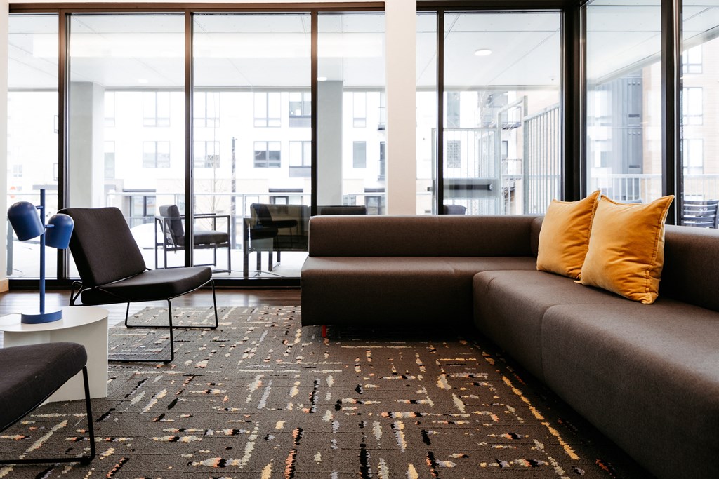 Indoor lounge area including a sectional couch and chairs next to large windows overlooking outdoor lounge area