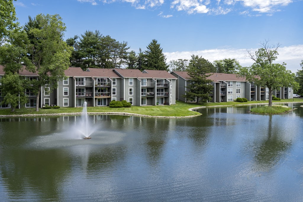 a fountain in the middle of a lake with an apartment building in the background