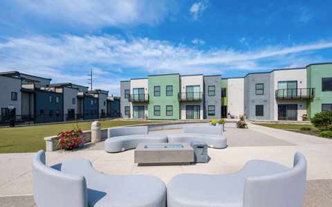 A modern outdoor seating area with white chairs and a bench in front of a row of colorful houses.