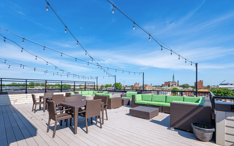 A rooftop patio with wooden flooring, tables and chairs, and string lights.