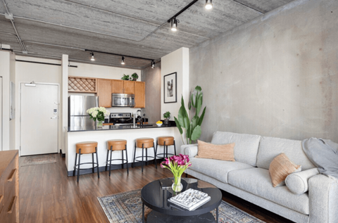 A modern living room with a grey couch and a kitchen area in the background.