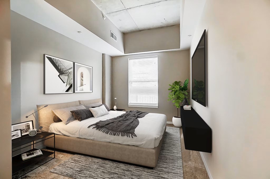 A bedroom with a bed, a nightstand, a plant, and a TV.