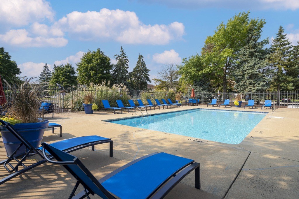 A pool surrounded by blue lounge chairs and trees.
