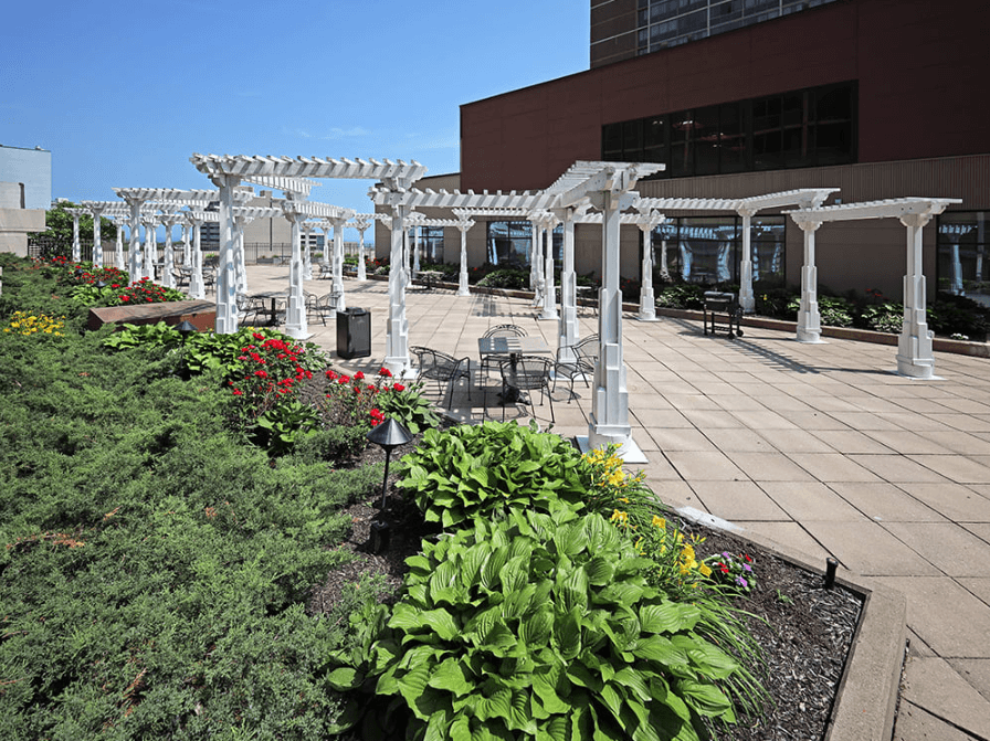 A white pergola is over a patio with tables and chairs.