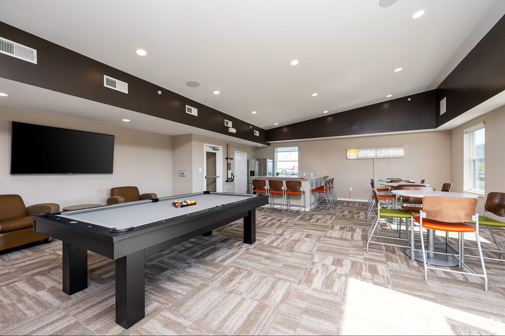 A room with a pool table and chairs.