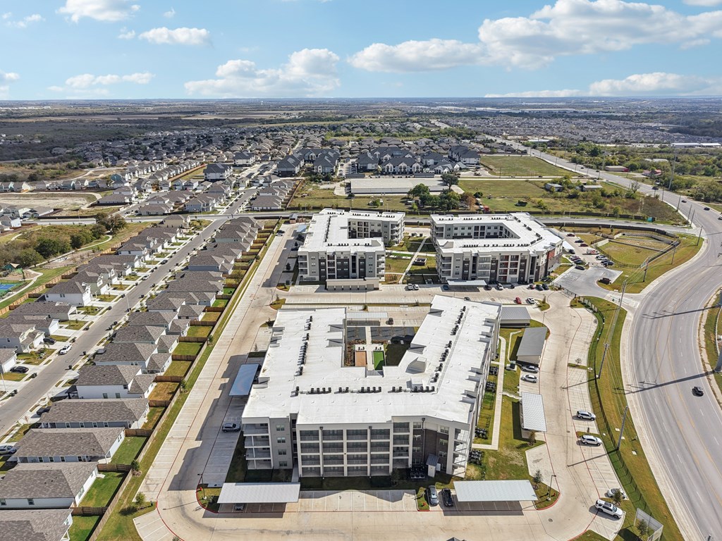A large, modern building complex is surrounded by a parking lot and residential houses.