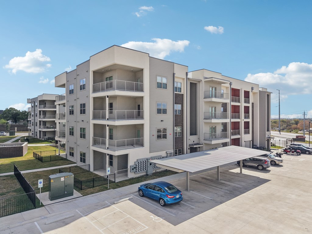 A blue car is parked in a parking lot in front of a large apartment building.