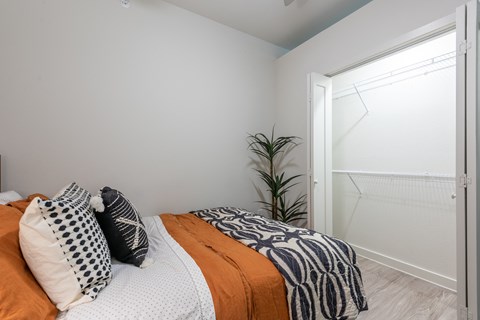 A bedroom with a bed covered in orange and white bedding and a plant in the corner.