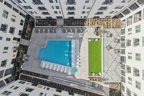A swimming pool is surrounded by a grassy area and concrete walkways. at ThreeTwenty at the Vybe Apartments, Kyle, 78640