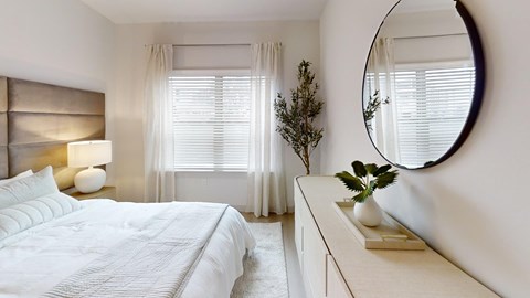 A bedroom with a large bed, a round mirror, and a nightstand with a plant on it.