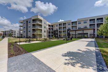 A sunny day at a modern apartment complex with a walkway and grassy area.
