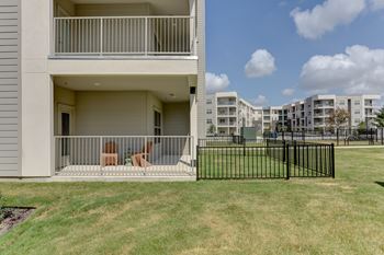 A balcony with chairs overlooks a grassy area in front of apartment buildings.