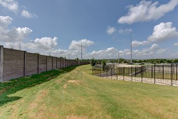 A long grassy field with a fence on one side and a pole on the other.