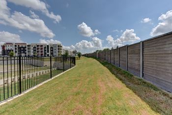 A long grassy path with a fence on one side and a building on the other.
