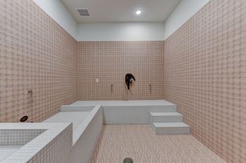 A person standing in a pink tiled bathroom with a white bench.
