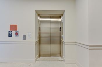 An elevator is in a hallway with a wall on the left.