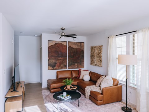 A living room with a brown leather couch and a painting on the wall.
