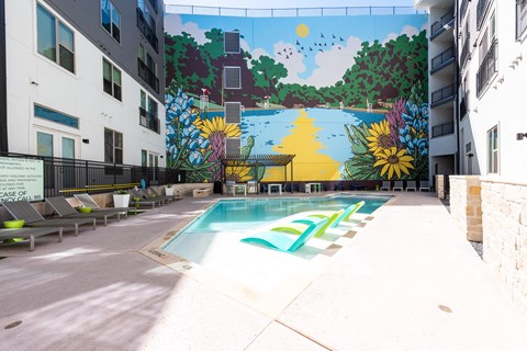A mural of a sunny day with trees and a river is painted on the wall above a pool.