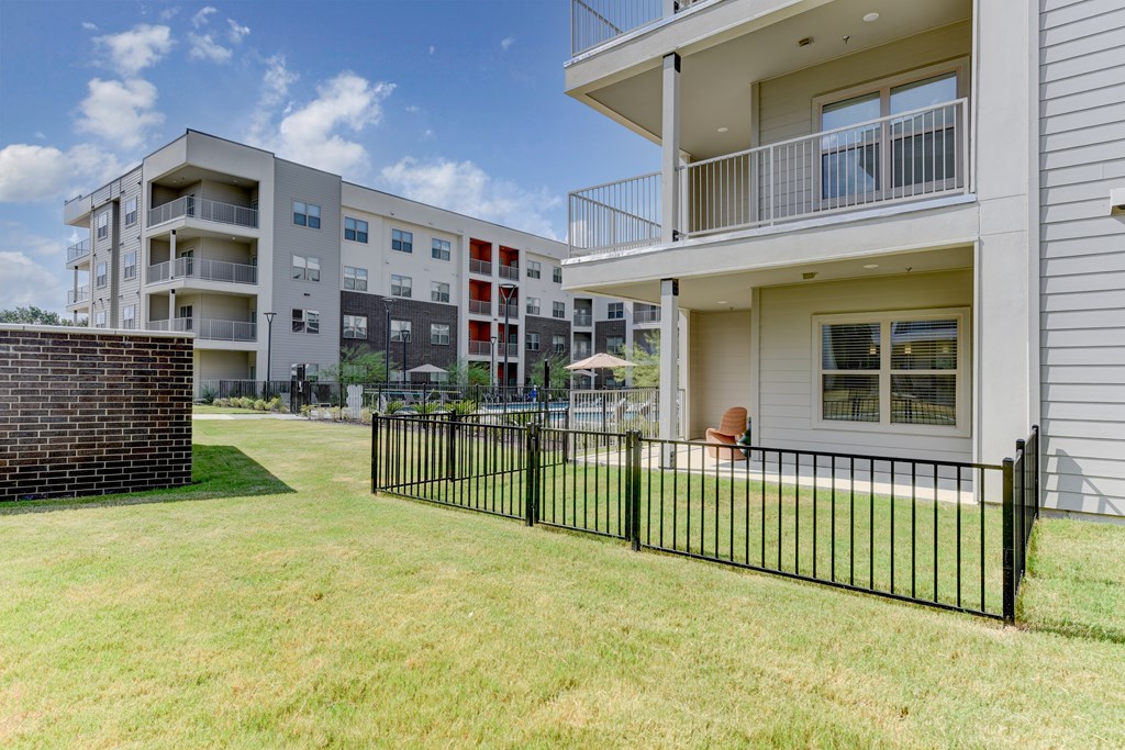 A black fence surrounds a grassy area in front of a modern apartment building.