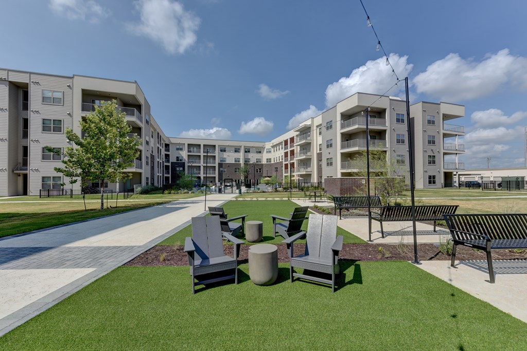 A grassy area with benches and a tree in front of apartment buildings.