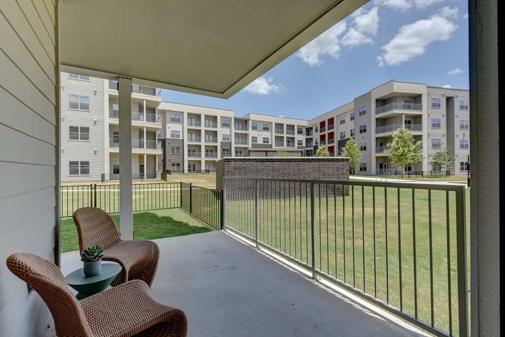 A patio with a table and chairs overlooks a grassy area and apartment buildings.
