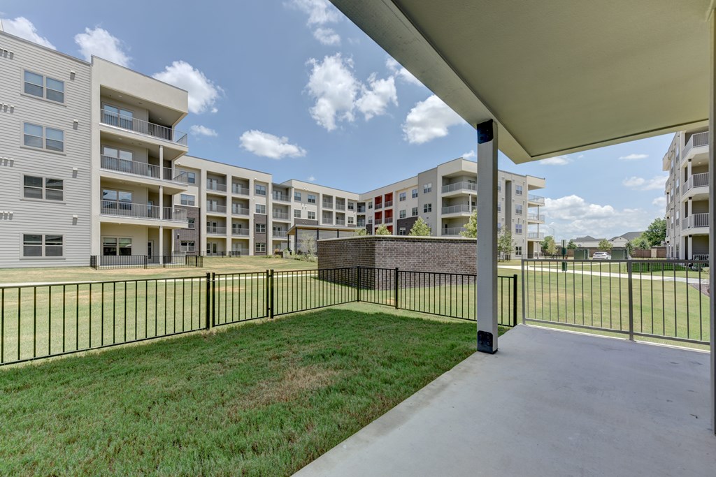 A view of a grassy area with a fence and apartment buildings in the background.