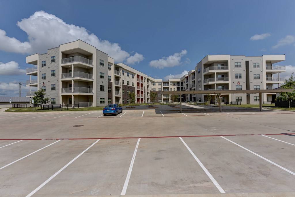 A parking lot in front of apartment buildings with a blue car parked in the lot.