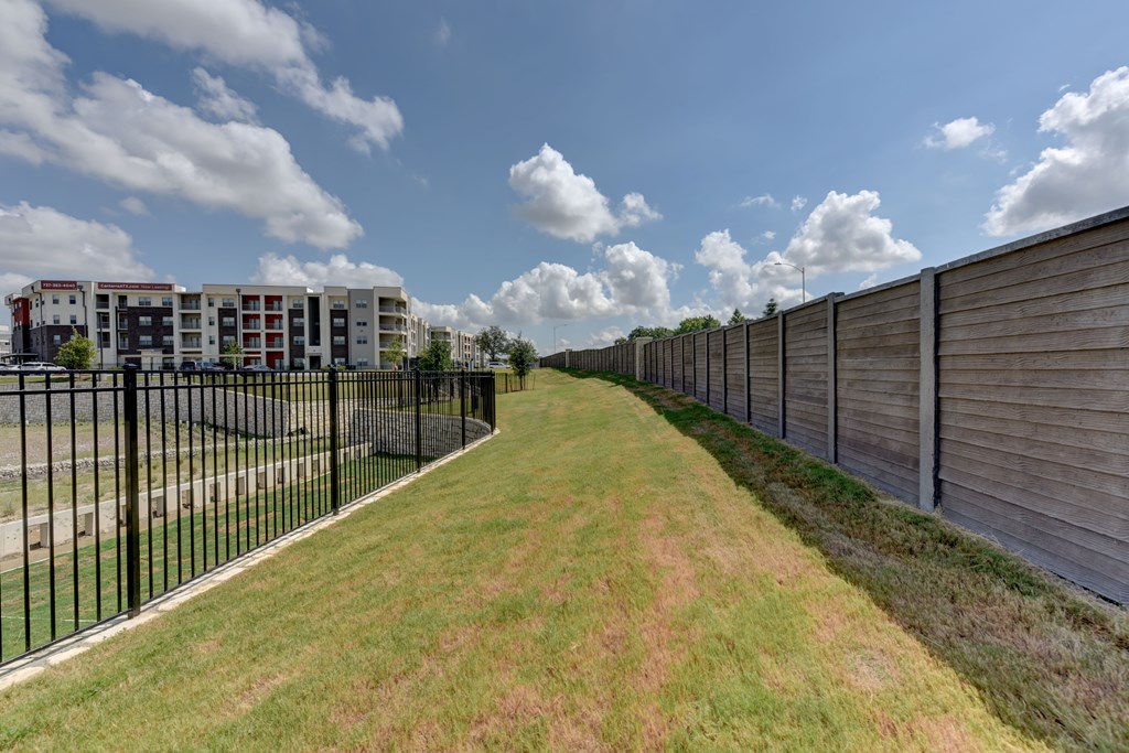 A long grassy path with a fence on one side and a building on the other.