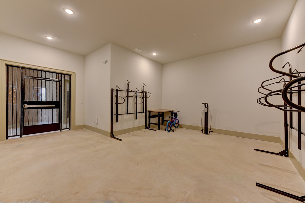 A room with a brown floor and white walls has a large open space with a few pieces of exercise equipment.